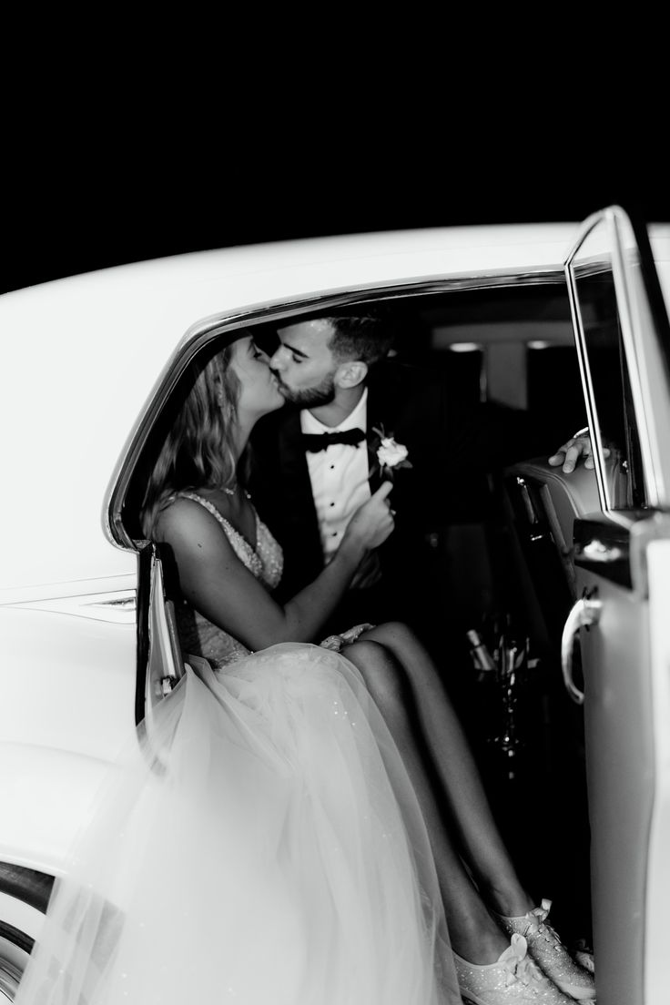 a bride and groom kissing in the back of a car