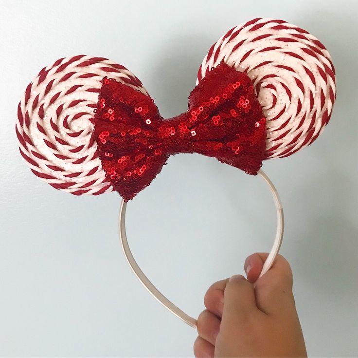 a hand holding up a red and white lollipop headband with sequins