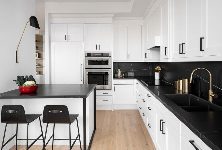 a kitchen with white cabinets and black counter tops, two bar stools next to the island