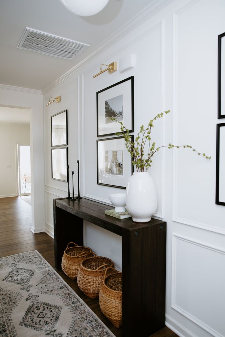 a hallway with white walls and pictures on the wall, two vases filled with flowers