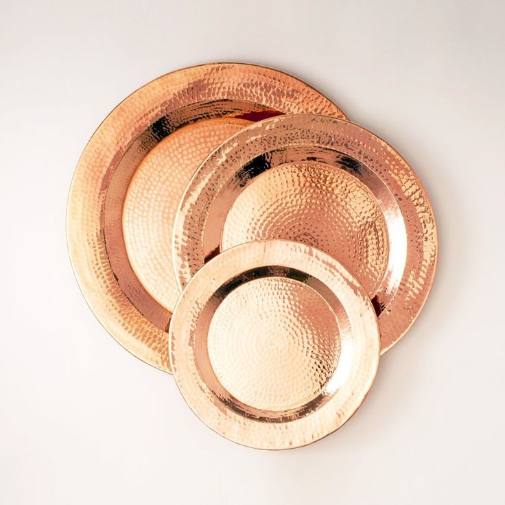 a set of four copper colored plates on a white surface