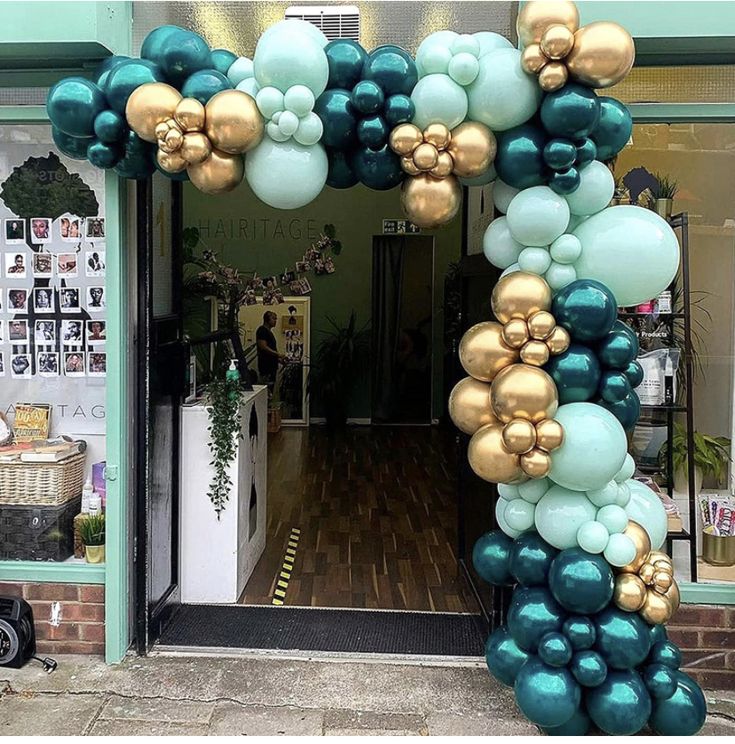 an arch made out of balloons in front of a storefront with blue and gold decorations