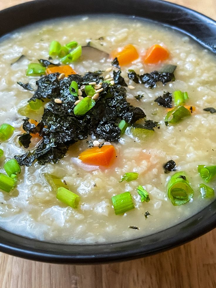 a black bowl filled with rice and vegetables on top of a wooden table next to a fork