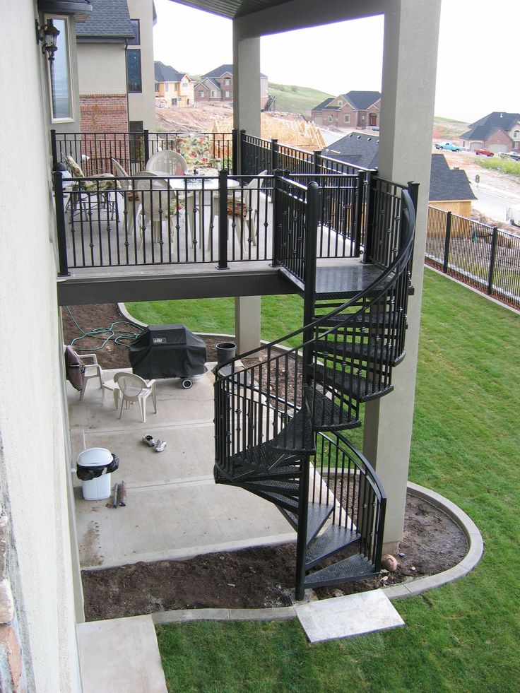 a black spiral staircase in the middle of a yard next to a building with lots of windows