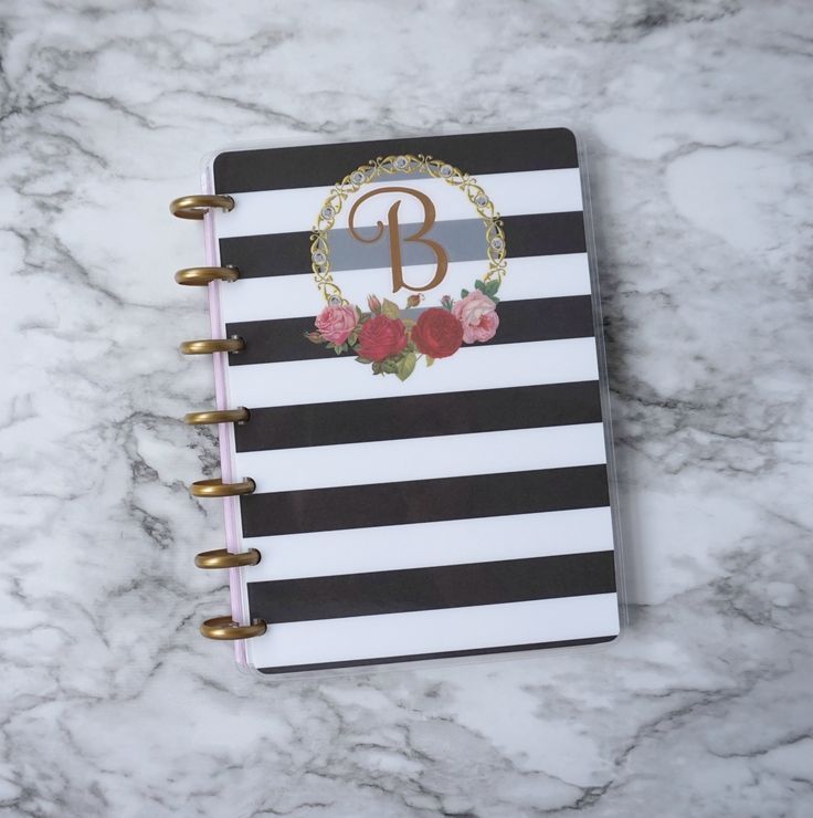 a black and white striped notebook with floral monogrammed initial on it, sitting on a marble surface