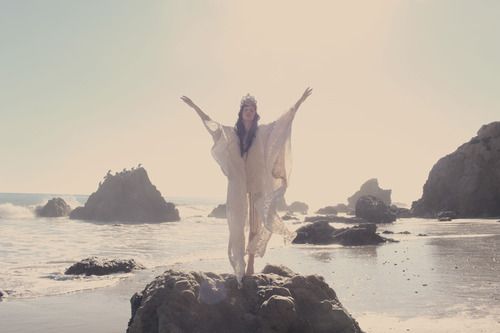 a woman standing on top of a rock next to the ocean with her arms in the air