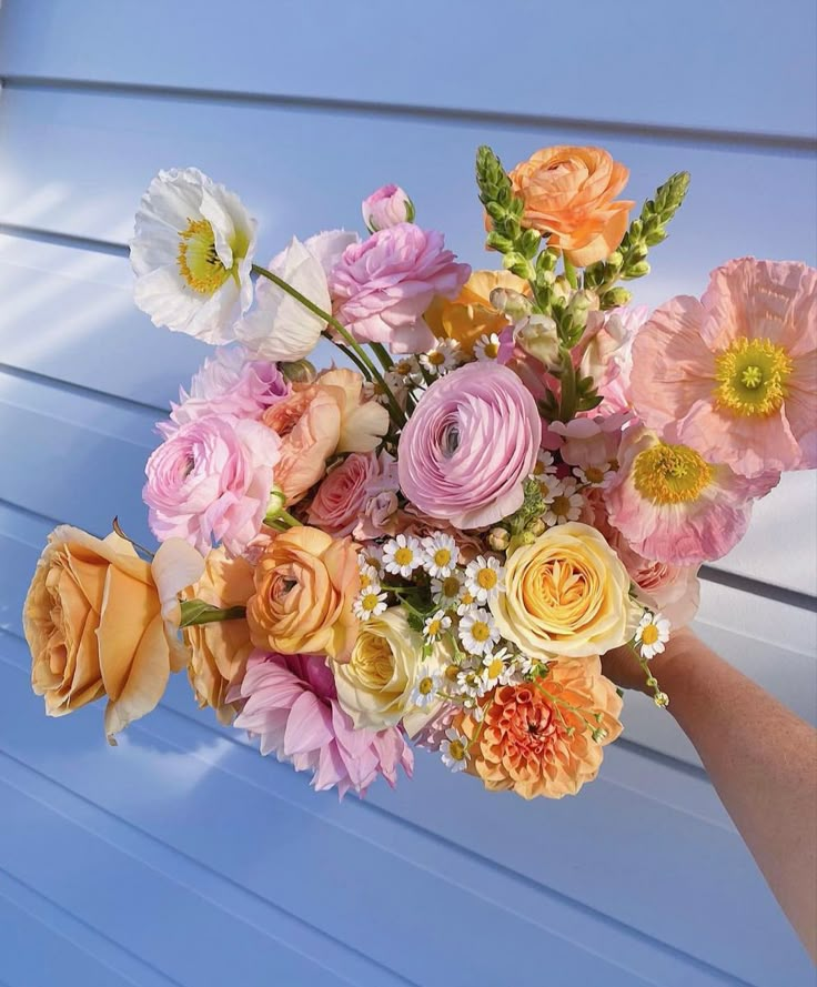 a person holding a bouquet of flowers in front of a blue wall with white and yellow stripes