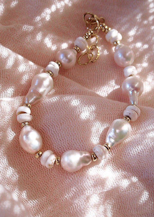 Flanked with luminescent natural white baroque pearls and puka shells, this unique luxurious bracelet evokes visions of Hawaii's white sands and soothing shores. Stack this with other beaded beauties and you'll be ready for your tropical escape.✦ DETAILS ✦✧ Name: Kakahi (ka KA hee) - Unique, outstanding, solitary.✧ Adjustable from 6.5"-8".✧ White Puka Shells.✧ Genuine Baroque Freshwater Pearls.✧ 14kt Gold Filled with lobster clasp.✧ All Ke Aloha Jewelry pieces come packaged thoughtfully, beautif Elegant White Shell With Pearl Chain, Elegant Shell Bracelet As A Gift, White Bohemian Bracelet With Pearl Charm, Bohemian White Bracelets With Pearl Charm, Bohemian White Bracelet With Pearl Charm, Bohemian White Shell With Pearl Charm, White Bohemian Shell With Pearl Charm, White Bohemian Jewelry With Oyster Bracelet, White Pearl Bracelet With Charm For Beach