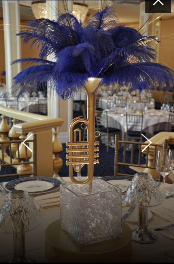 a table topped with a vase filled with blue feathers and a brass trumpet on top of it