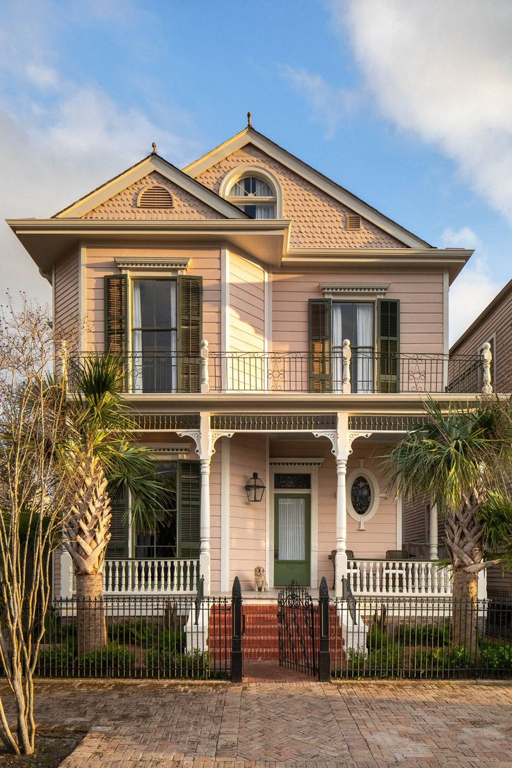 a large pink house with white trim and green shutters on the front door, surrounded by palm trees