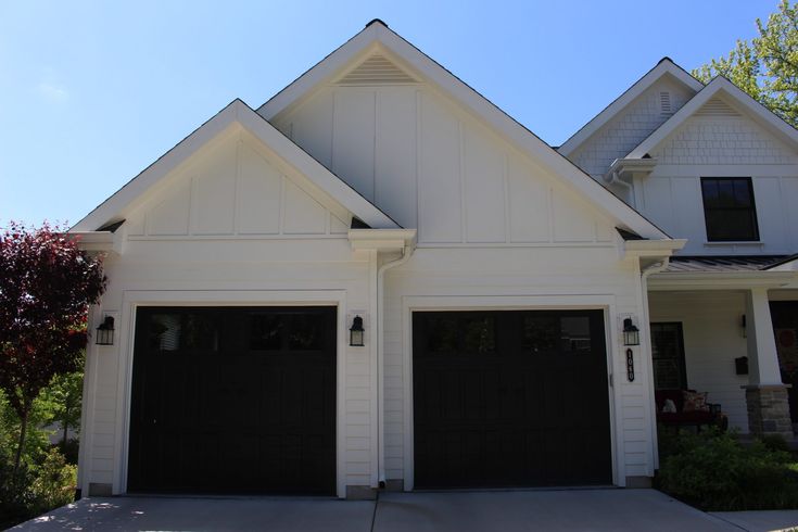 two black garage doors are on the front of a white house