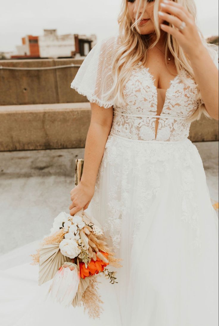 a woman in a wedding dress holding a bouquet and taking a selfie with her cell phone