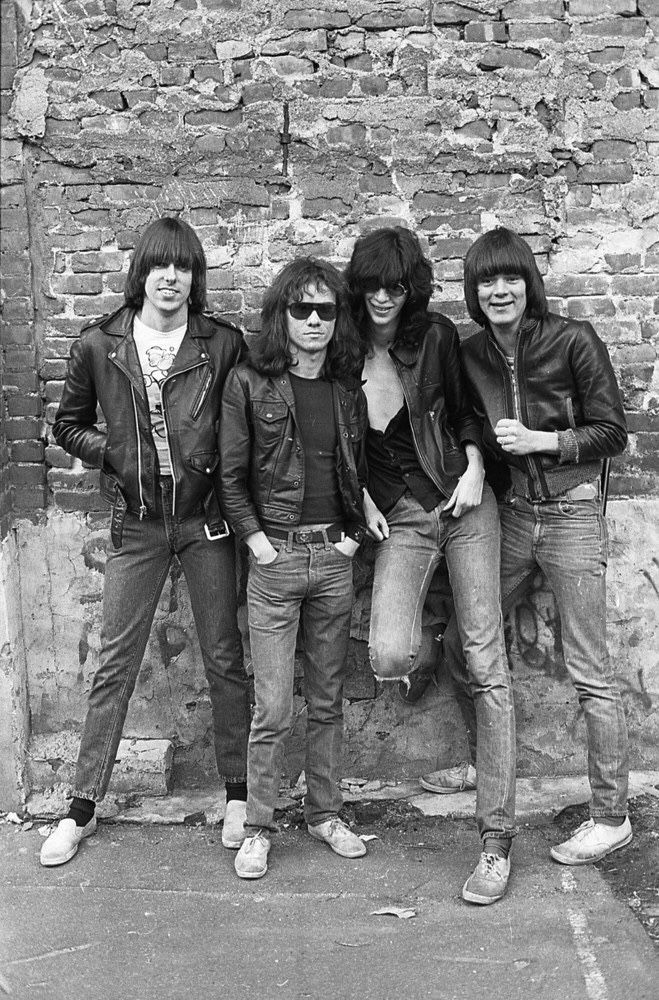 an old black and white photo of four young men standing next to each other in front of a brick wall