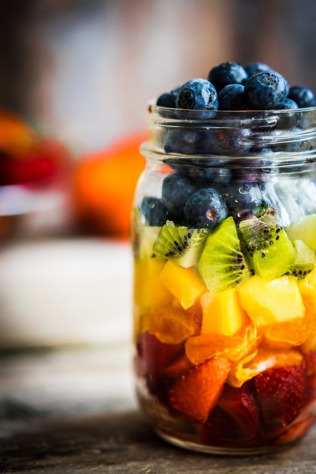 a glass jar filled with fruit salad on top of a wooden table