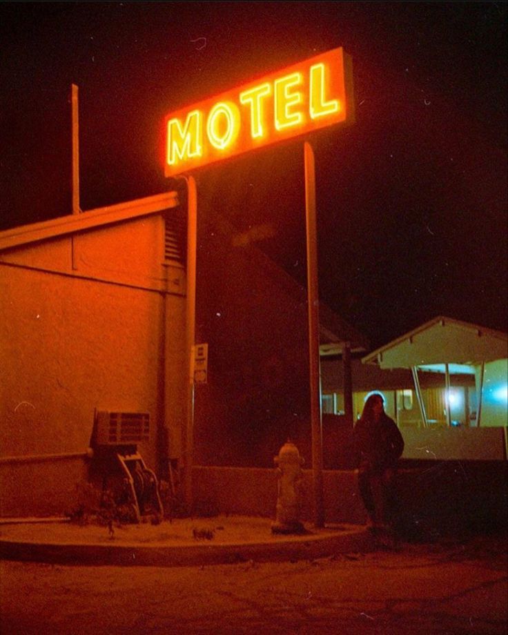 a motel sign lit up at night with people standing in the front yard and on the sidewalk