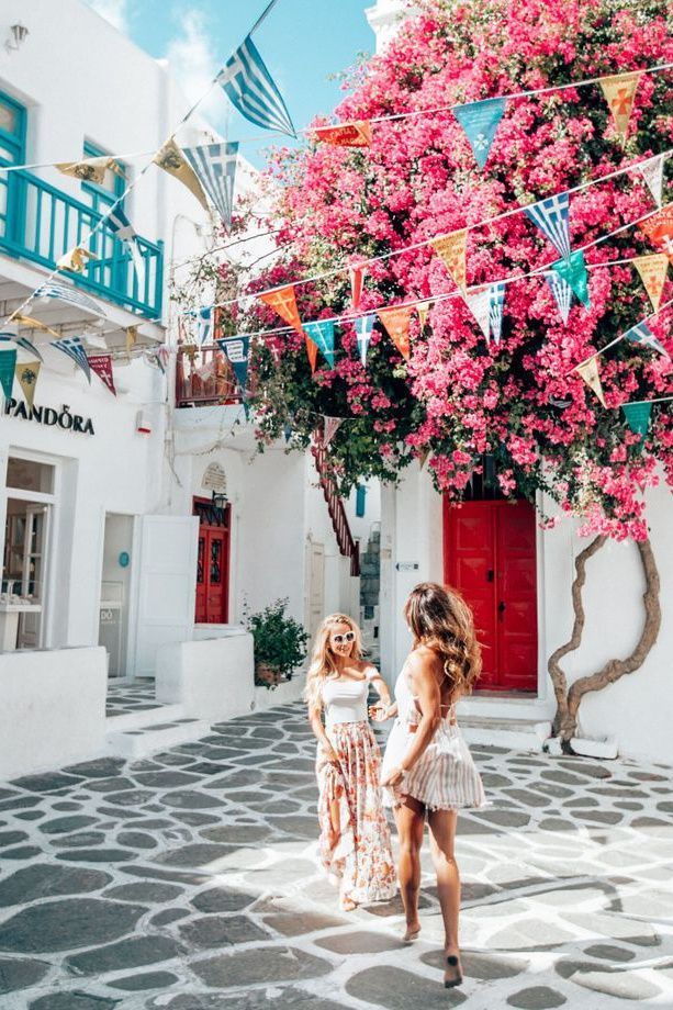 two women walking down the street in front of some buildings with colorful flowers on them