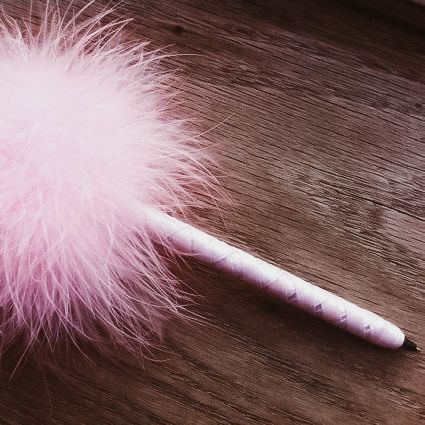 a pink feathered object sitting on top of a wooden table next to a pen