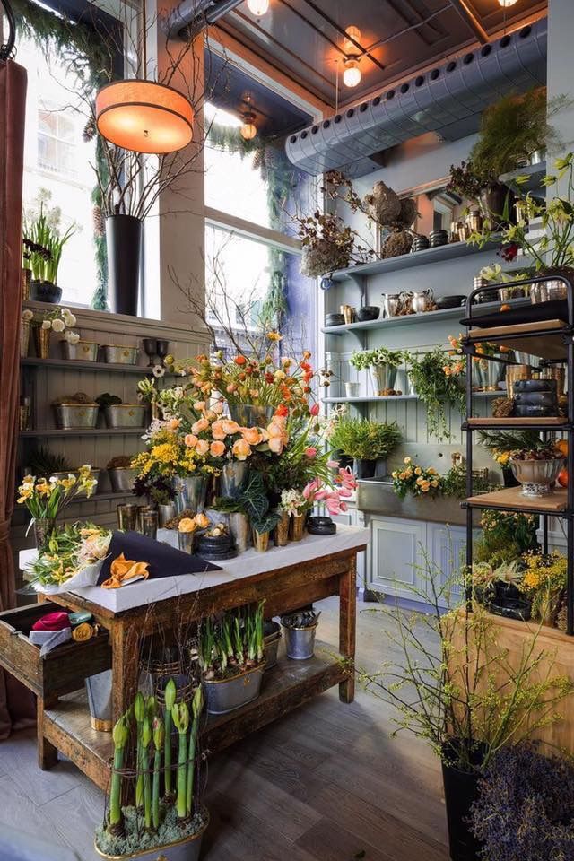 a room filled with lots of potted plants next to a wooden table covered in flowers