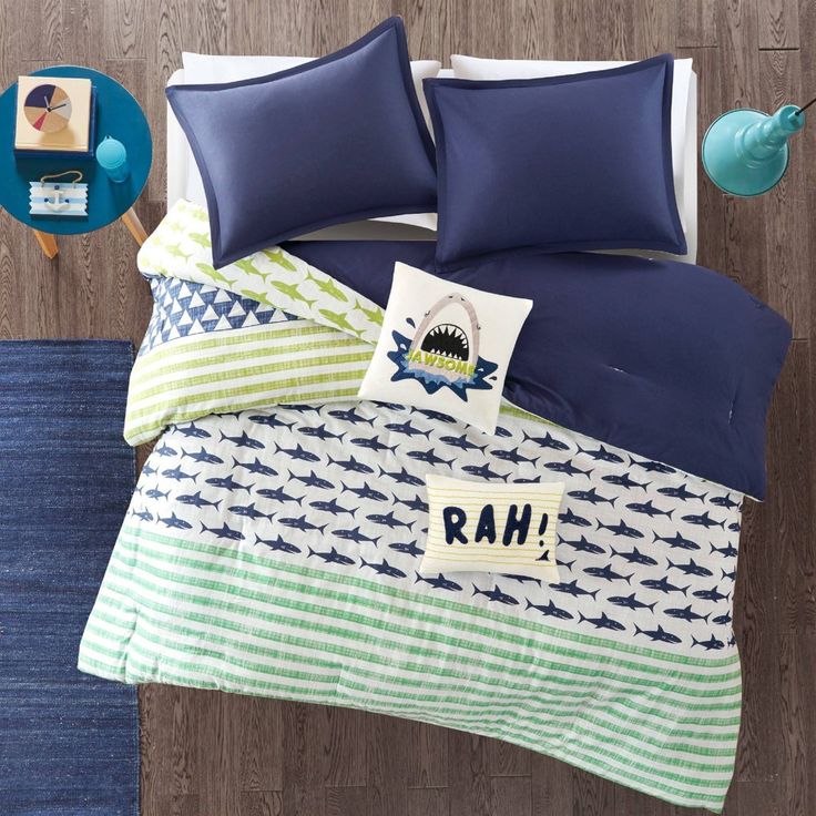 a bed with blue and green comforters on top of it next to a wooden floor