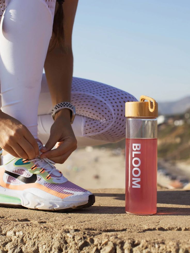 a woman tying her shoe laces next to a bottle of bloom water on the beach