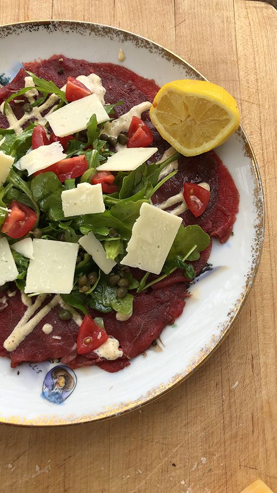 a white plate topped with meat and veggies next to a slice of lemon