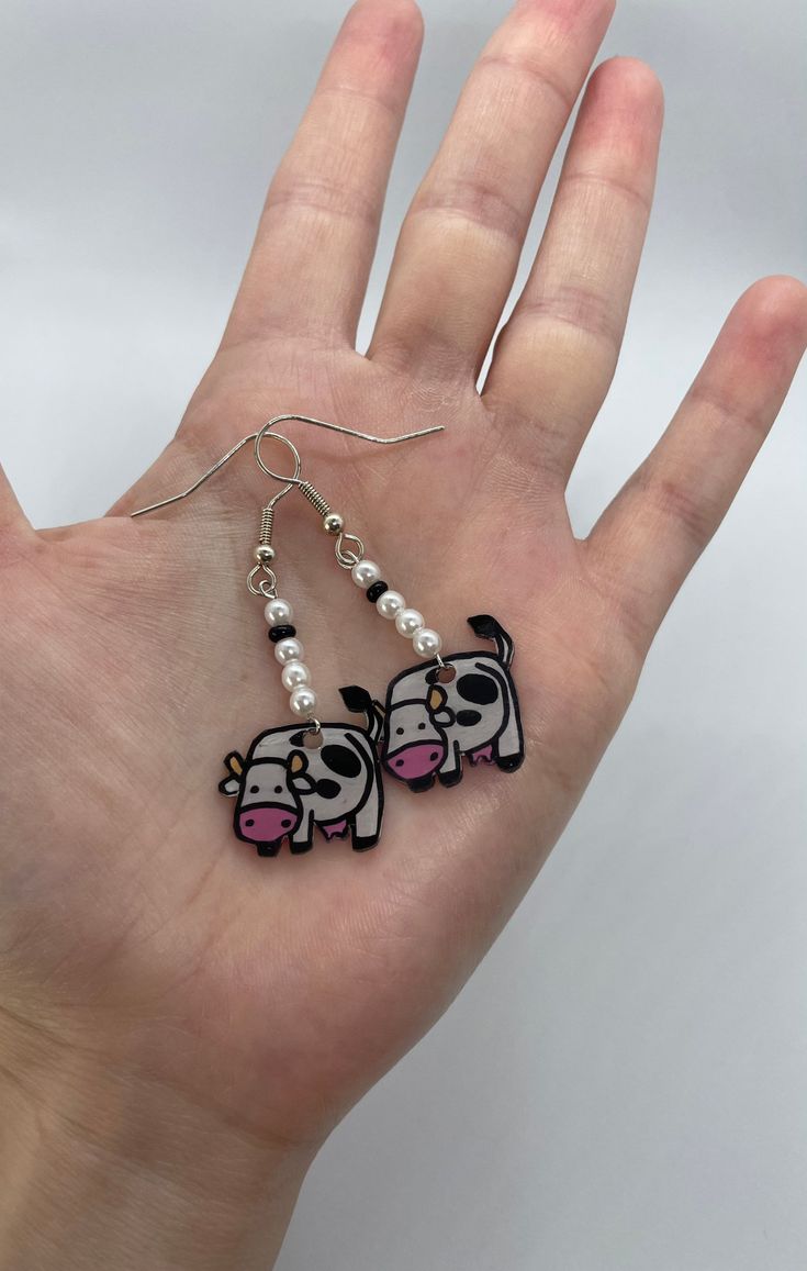 a person's hand is holding two small earrings with cartoon animals on them and pearls dangling from the ends