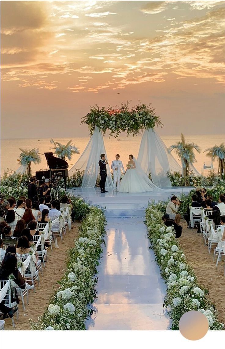 a wedding ceremony on the beach at sunset with people sitting in chairs and one person walking down the aisle