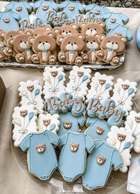 baby shower cookies are arranged on a table with teddy bears and blue onesuits