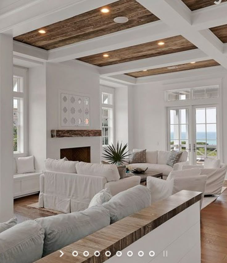 a living room filled with white furniture and wooden beams on the ceiling, along with large windows