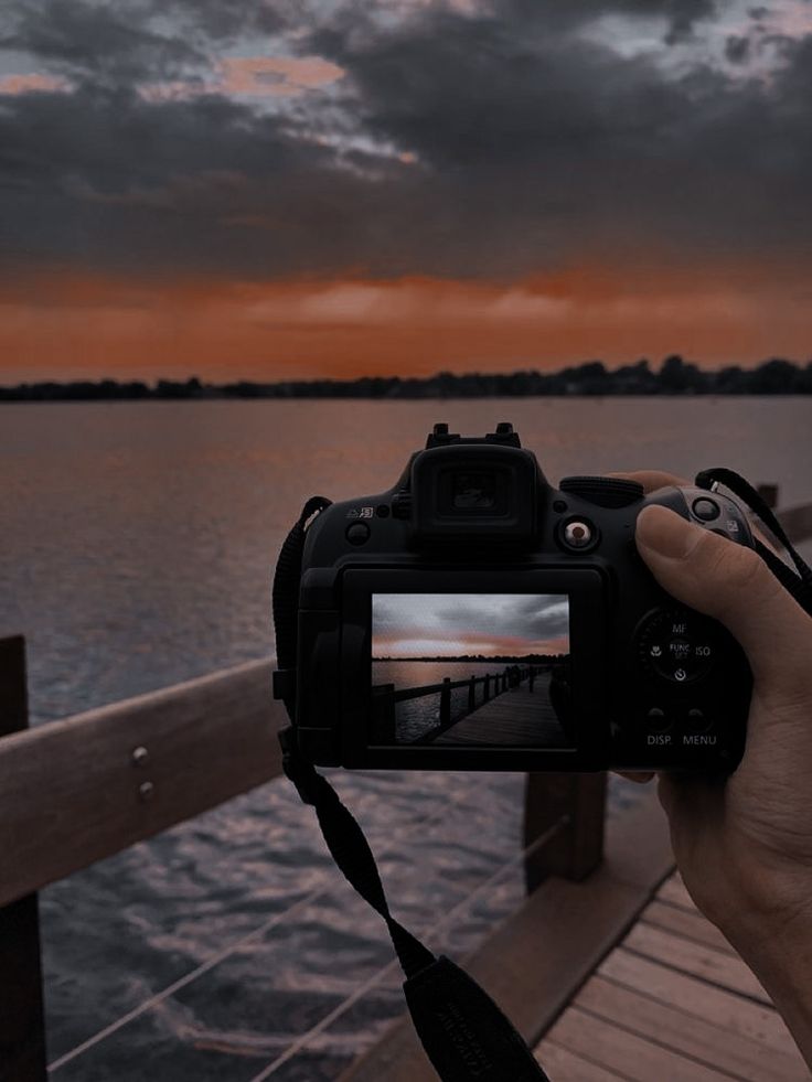 a person holding up a camera to take a photo on a pier at sunset or dawn