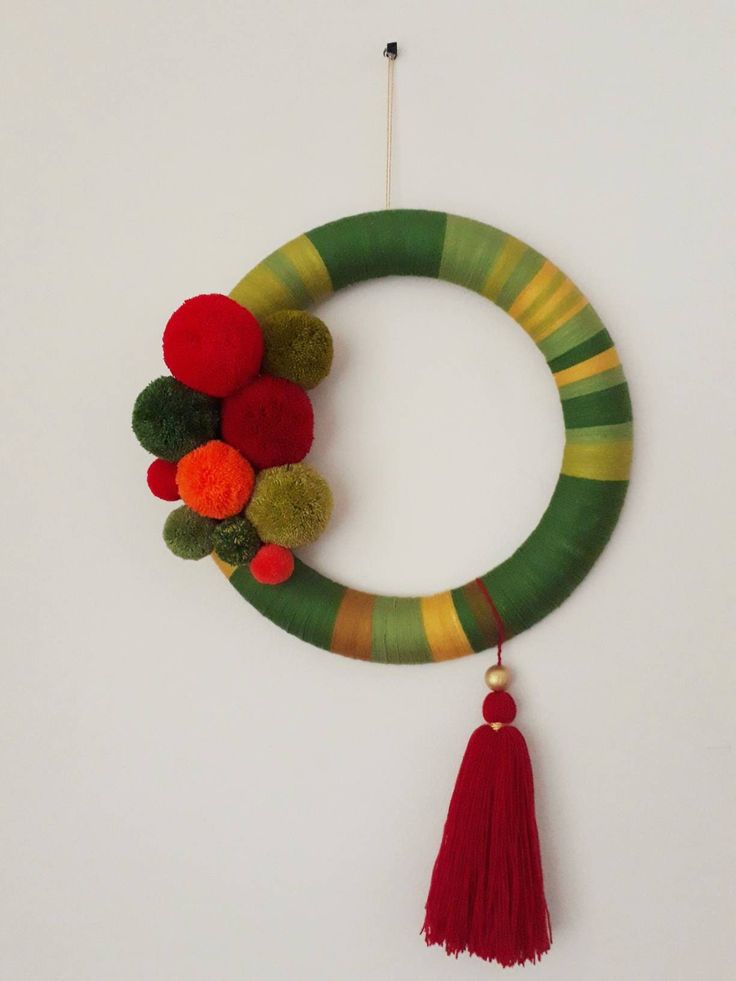 a green and red wreath with pom - poms hanging from it