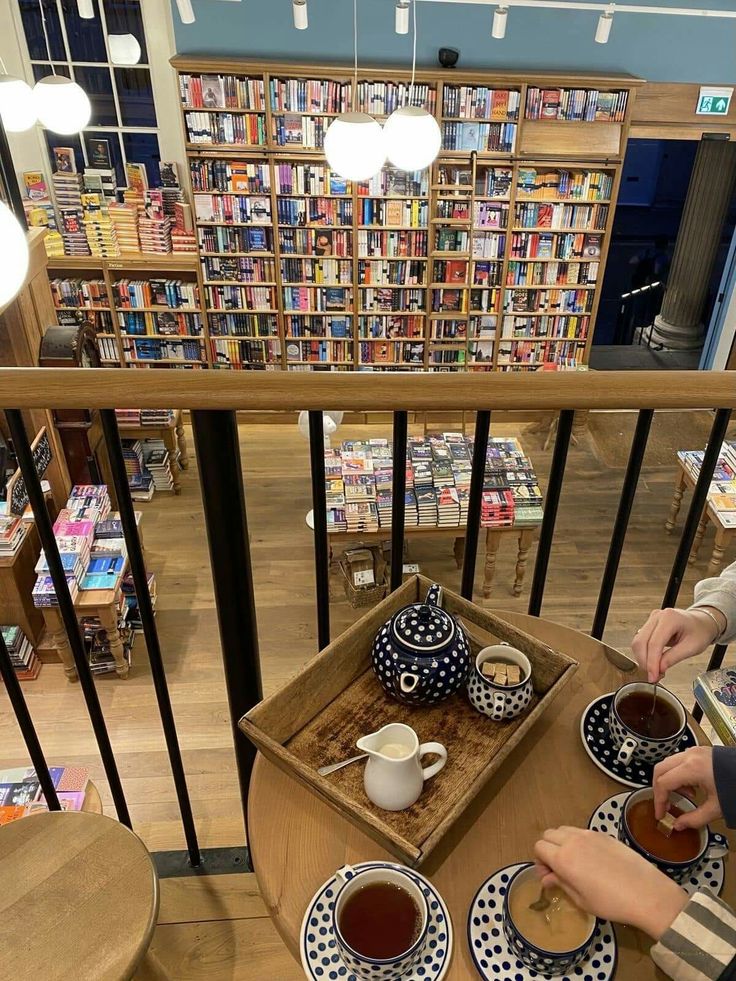 two people sitting at a table with plates and cups of tea in front of bookshelves