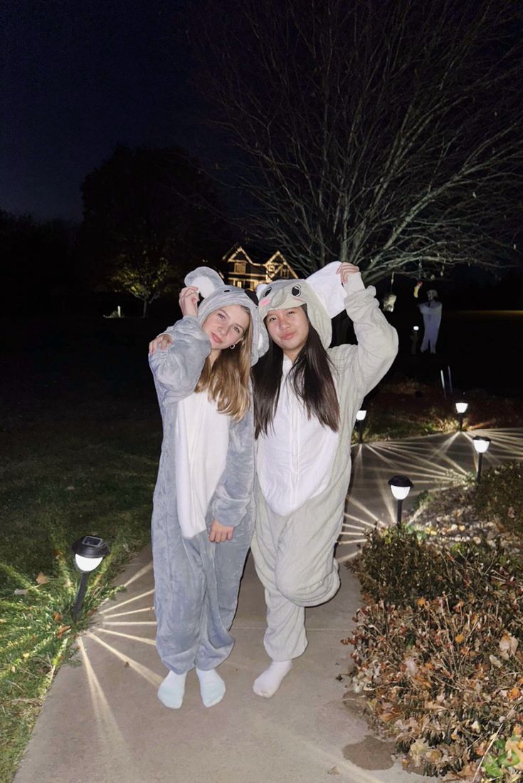 two girls dressed in animal onesuits posing for the camera at night with their arms around each other