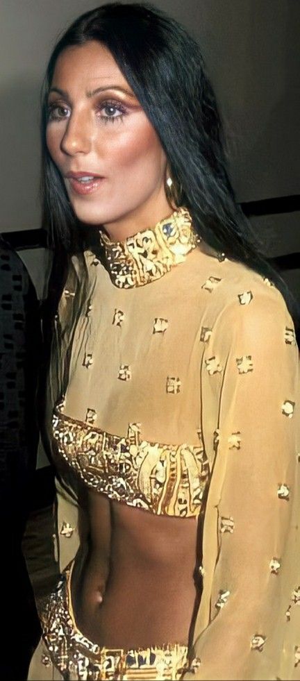 a woman with long black hair wearing a gold outfit