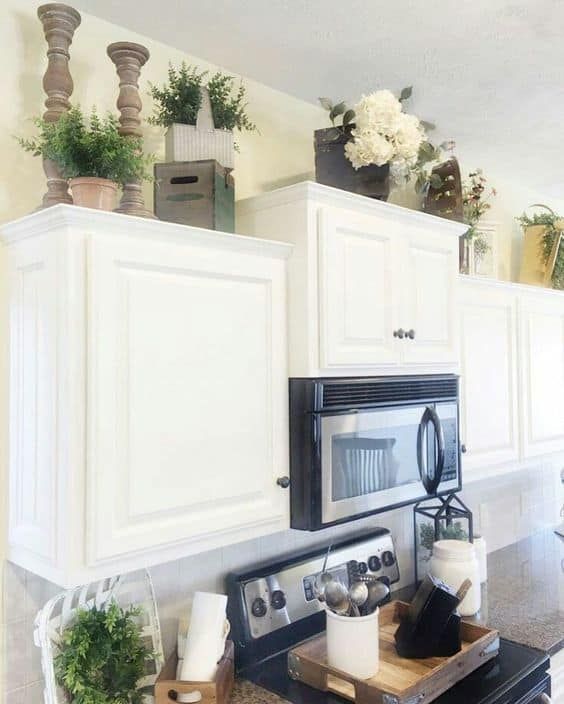 a kitchen with white cabinets and black stove top oven, potted plants on the counter