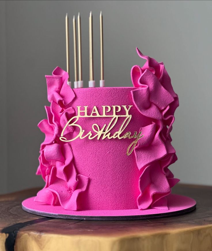 a pink birthday cake with gold lettering and ruffles