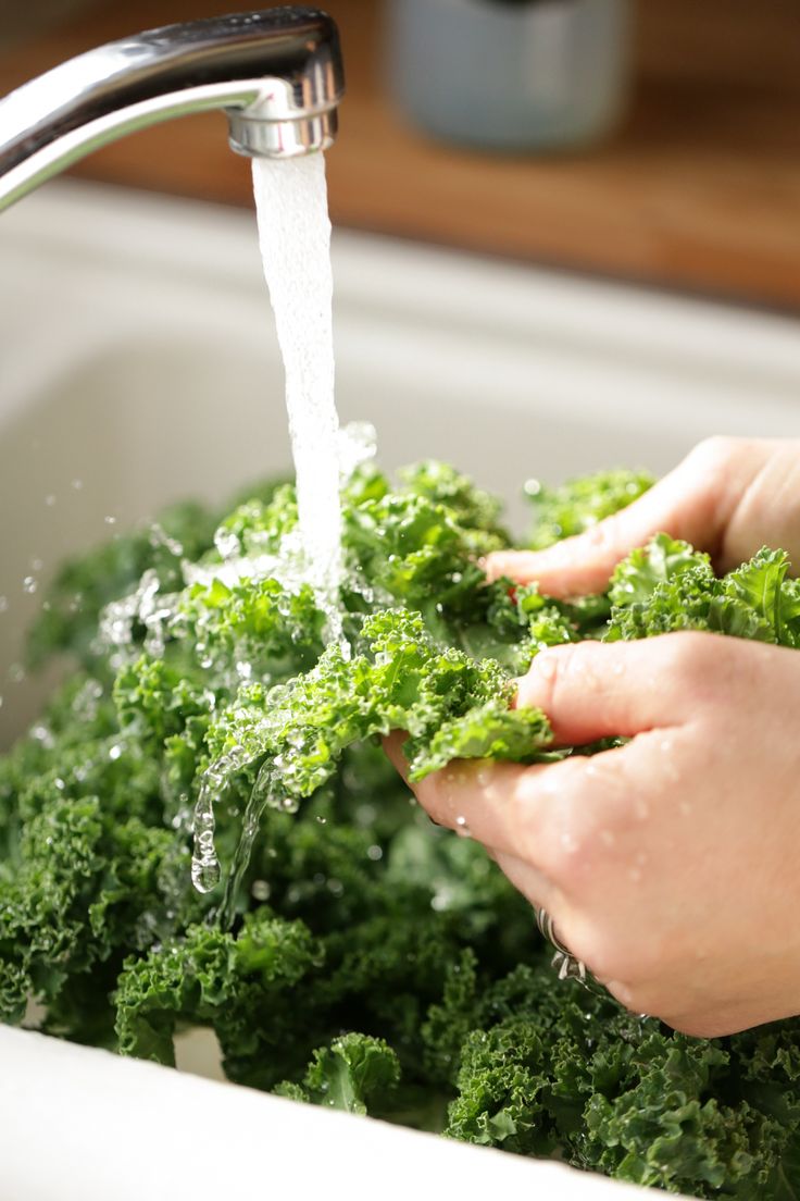 a person is washing their hands with some green vegetables in the sink and water coming out of the faucet