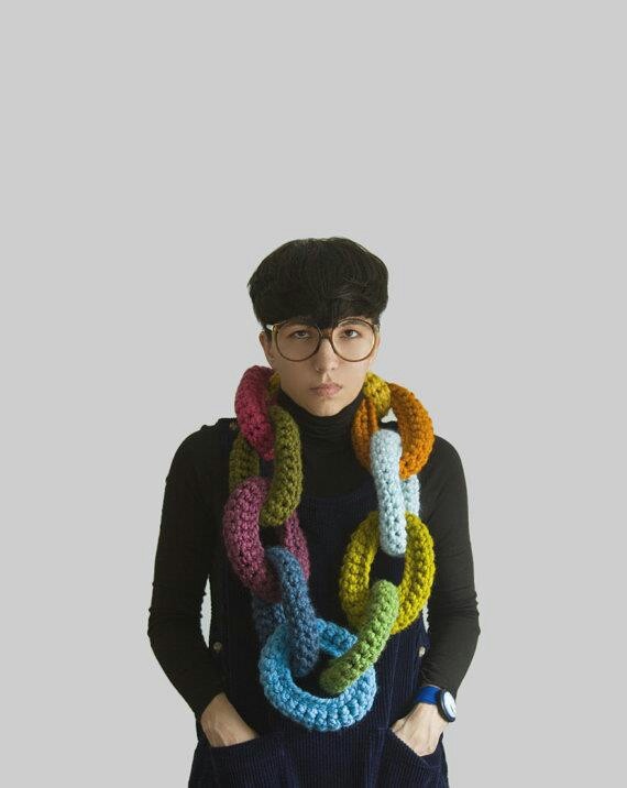 a woman standing with her hands on her hips wearing a multicolored crocheted scarf