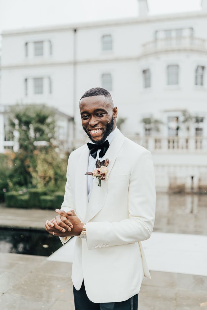 a man in a white tuxedo smiles at the camera while holding his hands together