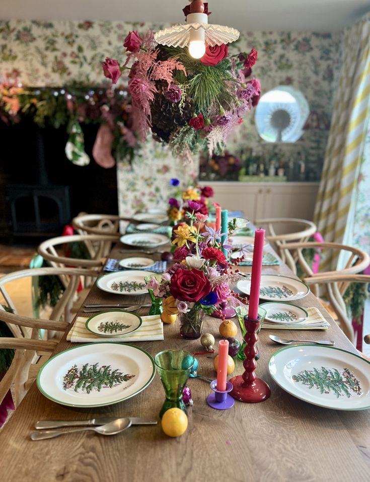 the table is set with plates, candles and flowers on it for a festive dinner