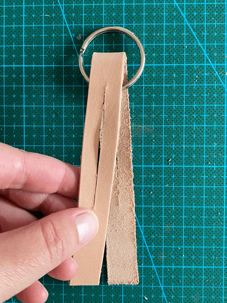 a person is holding a piece of wood in front of a green cutting mat with a pair of scissors