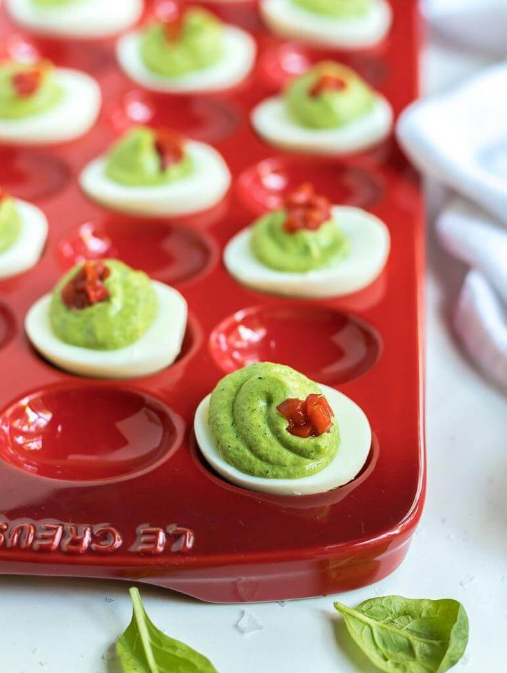 deviled eggs with guacamole in the middle on a red tray next to green leaves