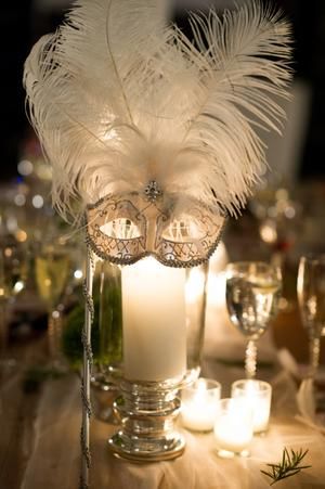 a candle and some white feathers on a table with candles in the centerpieces