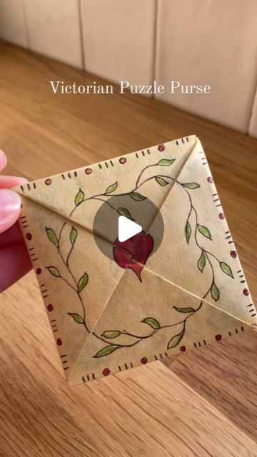 someone is holding an origami envelope with leaves and berries on it, in front of a wooden table