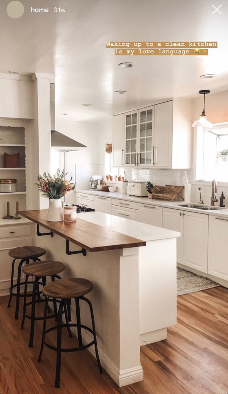 a large kitchen with white cabinets and wooden flooring, along with two stools at the island