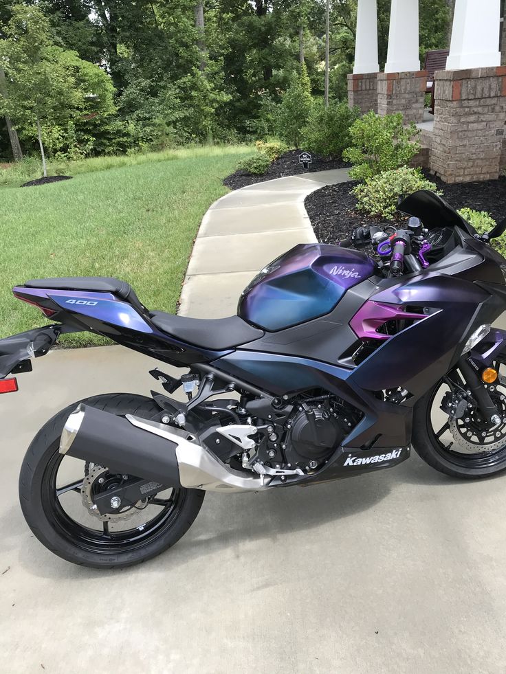 a purple and black motorcycle parked on top of a driveway next to a sidewalk with trees