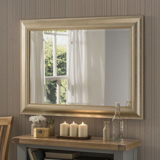 a mirror on the wall above a table with some candles and a vase in front of it