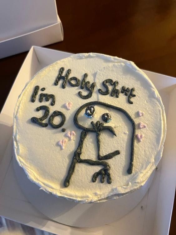 a white cake with black writing on it sitting in a box next to a knife and fork