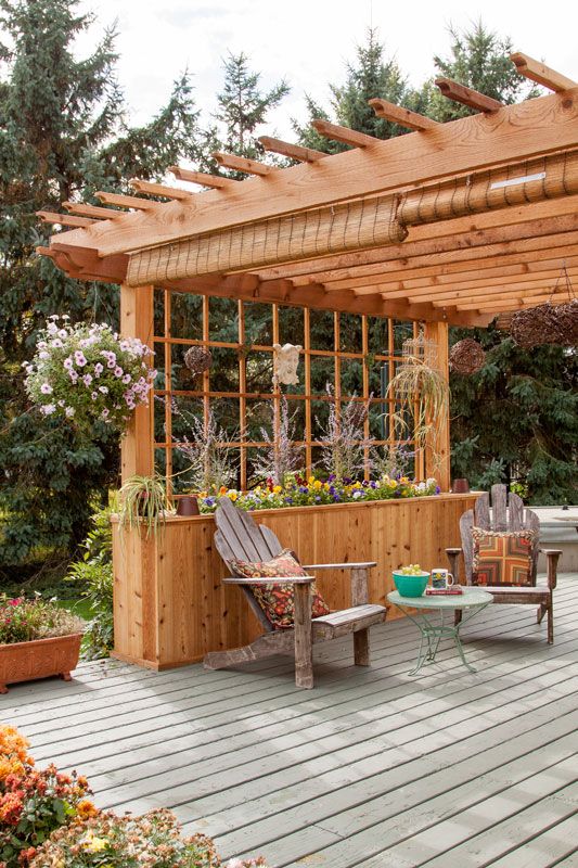 a wooden deck with chairs and tables under a pergolated roof covered in plants