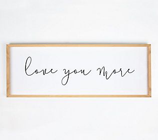 a framed sign that says, love you more on the wall next to a potted plant